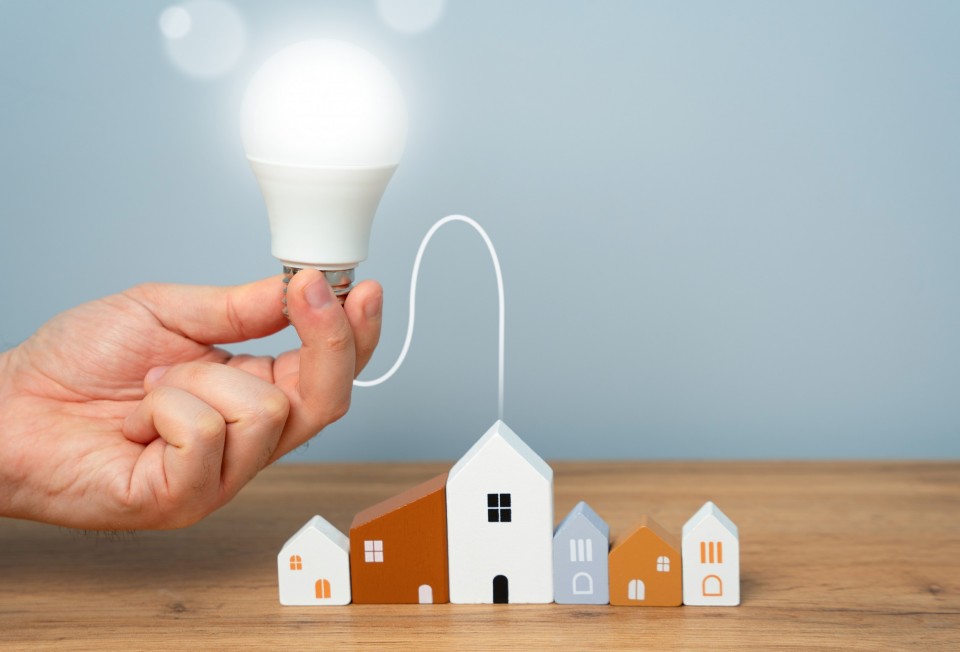 hand-connects-light-bulb-to-residential-buildings-2025-03-18-17-08-27-utc